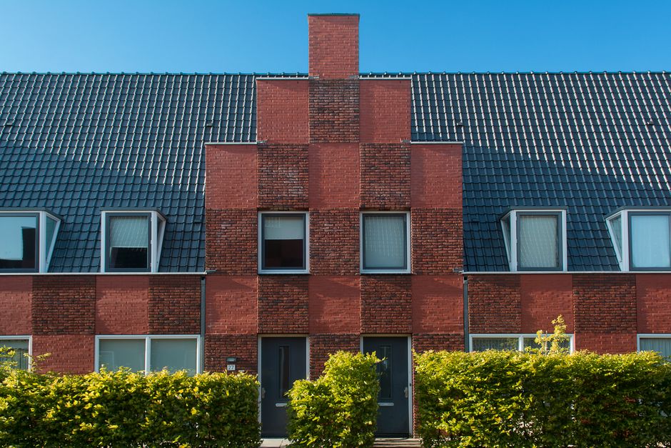 Contemporary brick townhouse facade with neat hedge under clear blue sky.